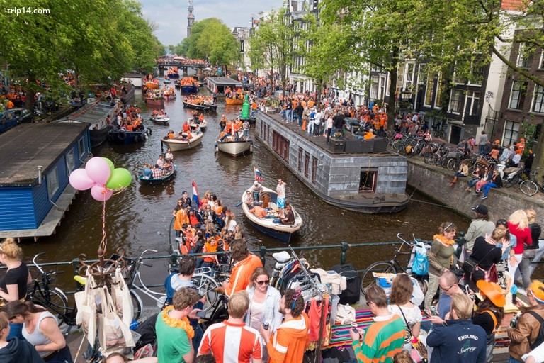 Đám đông ăn mừng Koningsdag, Lễ hội Kings Day ở Amsterdam với những chiếc thuyền trên kênh Prinsengracht và Vrijmarkt trên cầu. - Trip14.com