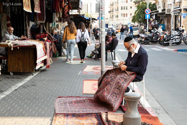 Một người bán thảm đang sửa một tấm thảm trên đường trước cửa hàng của anh ta ở chợ trời nổi tiếng - Trip14.com